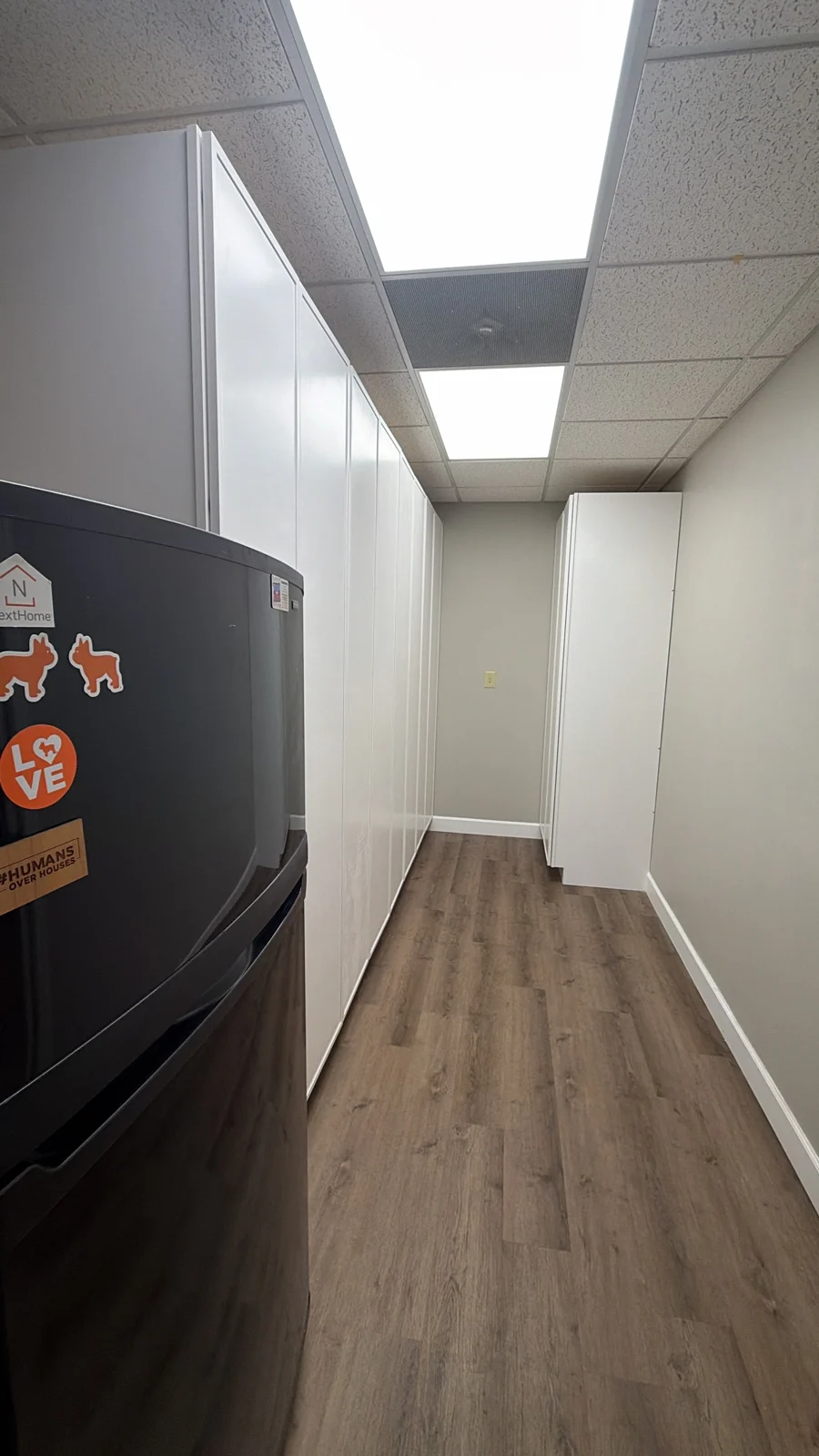 Tall white office storage cabinets fitted along a breakroom wall beside a refrigerator